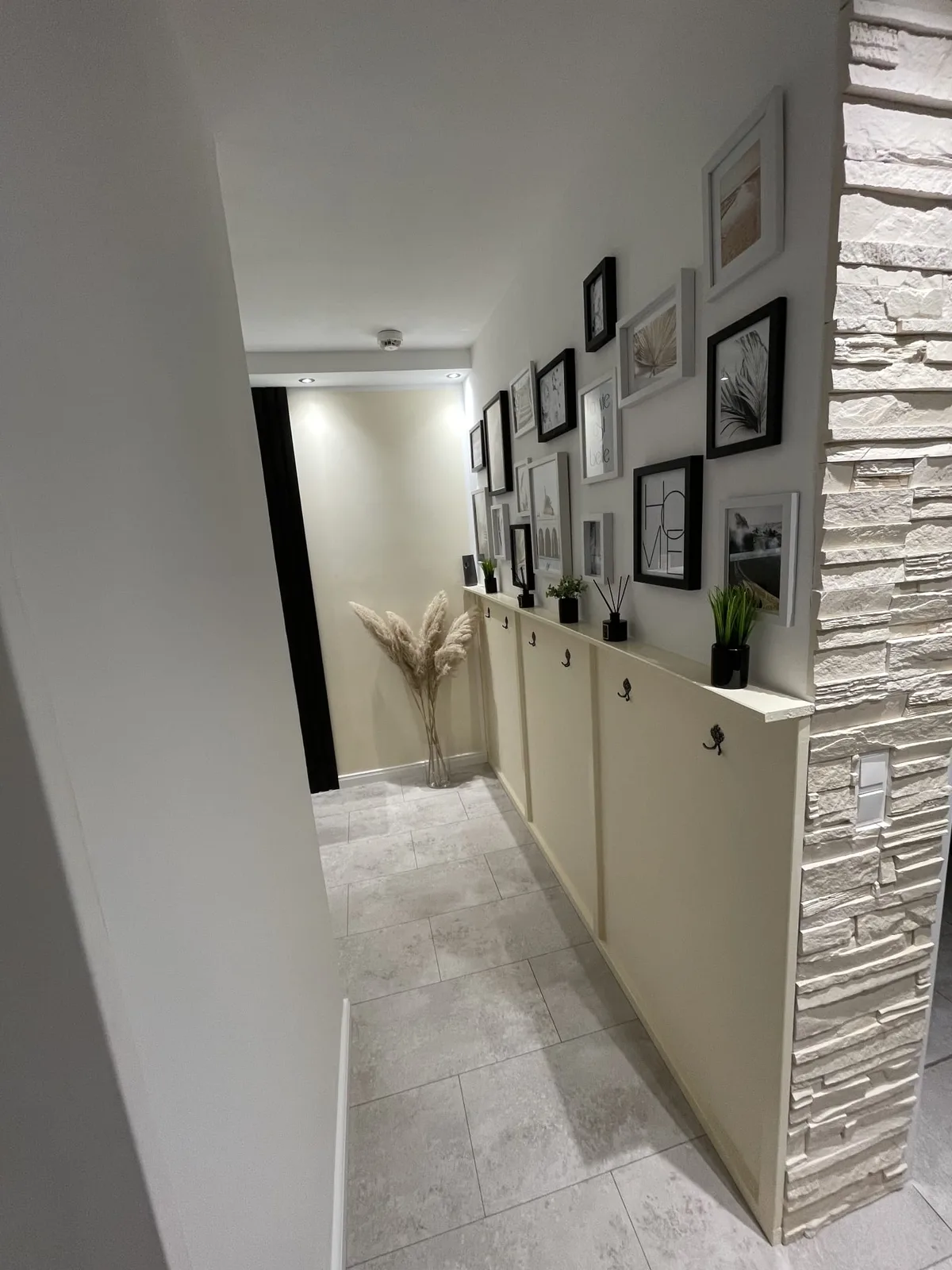 Flur nach der Wandgestaltung mit weißer Steinverblendung, Bilderwand und Garderobe